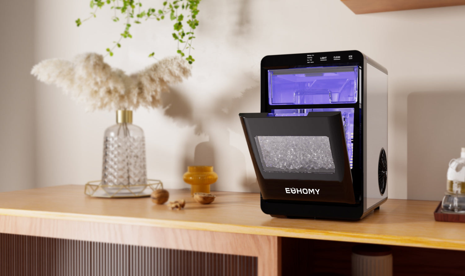An EUHOMY ice maker with its door open, placed on a wooden countertop next to decorative items.
